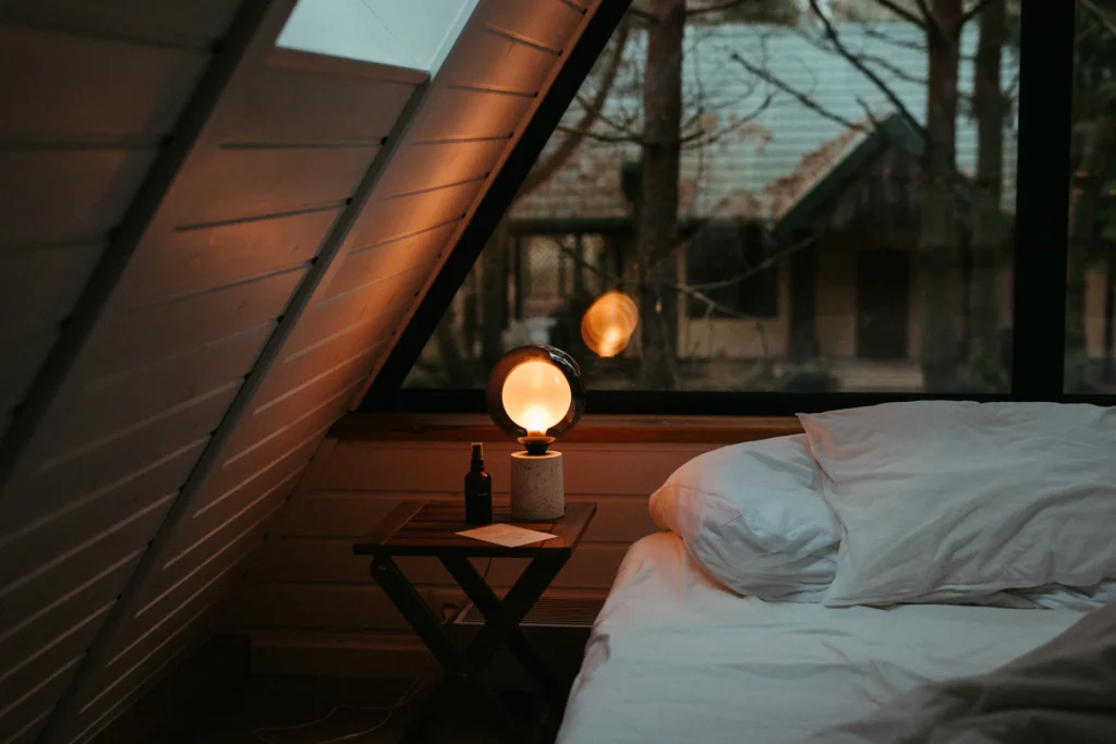 Łóżko pod oknem i zapalona lampka nocna wieczorem